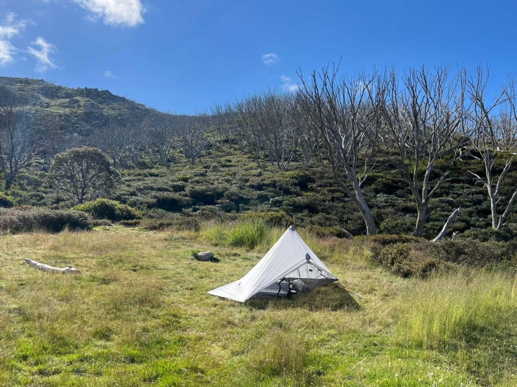 A white ultralight tent pitched on flat, grassy terrain in a designated camping area to minimise environmental impact.