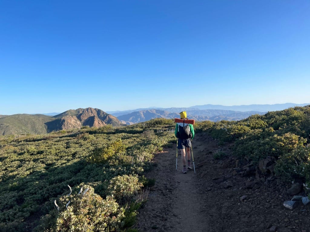 A hiker walking on a well-established trail under a clear blue sky.